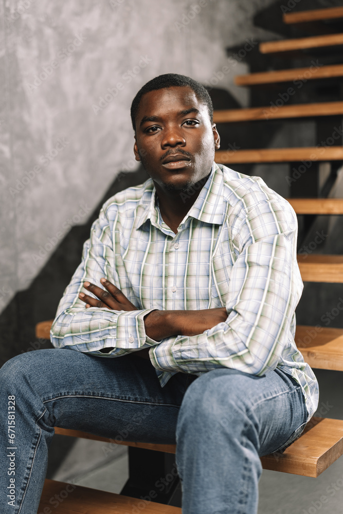 Young african man sitting on a wooden ladder in a room, portrait Young african man sitting on a wooden ladder in a room, portrait
