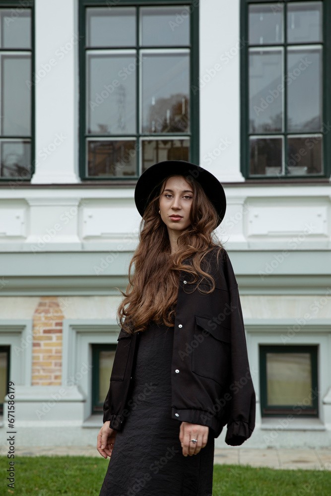 Attractive young  fashionable woman posing in black hat and jacket, outside portrait.