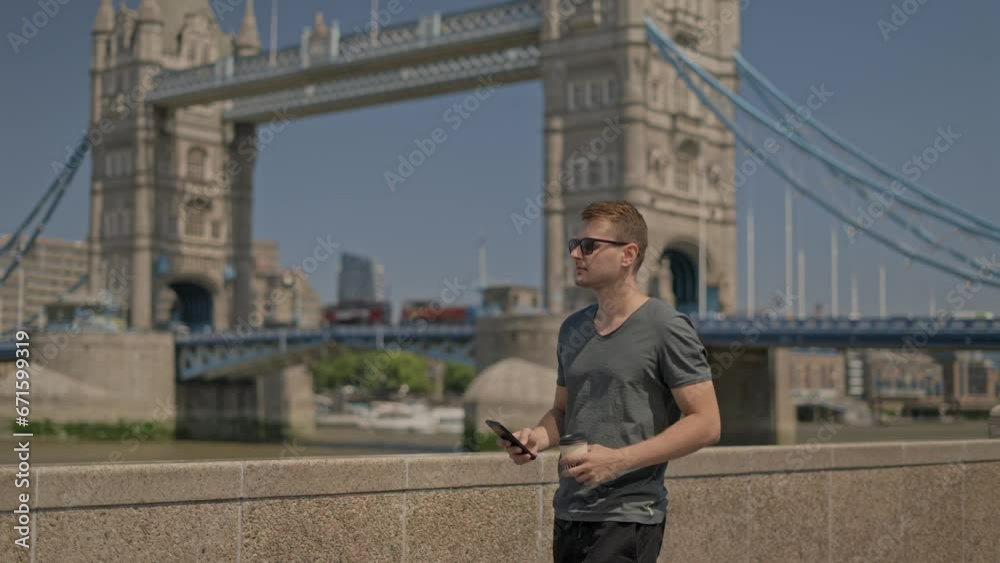 Young man tourist enjoying drinking coffee by the Tower Bridge, city of London skyline, on a beautiful sunny morning Young man tourist enjoying drinking coffee by the Tower Bridge, city of London skyline, on a beautiful sunny morning