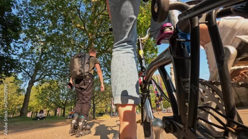  Low angle of woman pedalling bike in the park in London, close up of bike gear. Bicycle wheel rotation view. Cyclist twists pedals on bicycle on cycle path