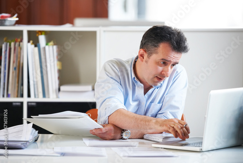 Business man, laptop and documents with reading, scroll and thinking with finance review, budget or audit. Accountant, computer and paperwork for financial compliance in office, process and solution © Marine G/peopleimages.com