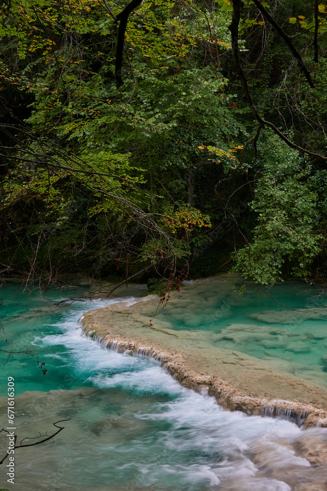 Obraz premium The waterfalls and crystal clear, blue, turquoise and green waters of the Nacedero del Urederra, with its beech forest with its autumn colors in the Sierra de Urbasa-Andía. Navarre. Spain