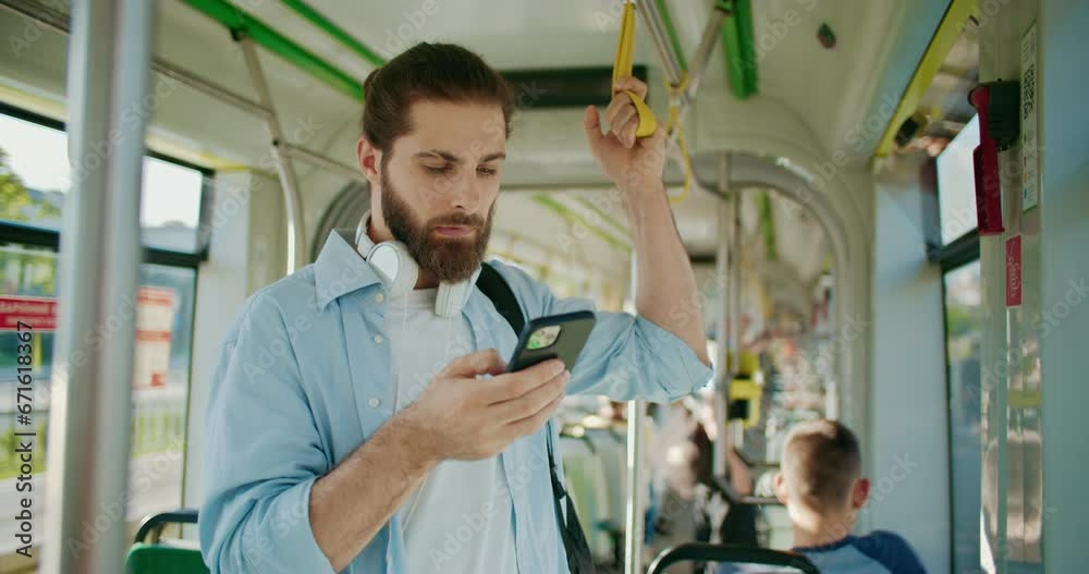 Male young traveler with backpack using smartphone to surfing internet or scrolling social networks. Handsome guy riding in public transport, standing inside bus and recording voice messages.