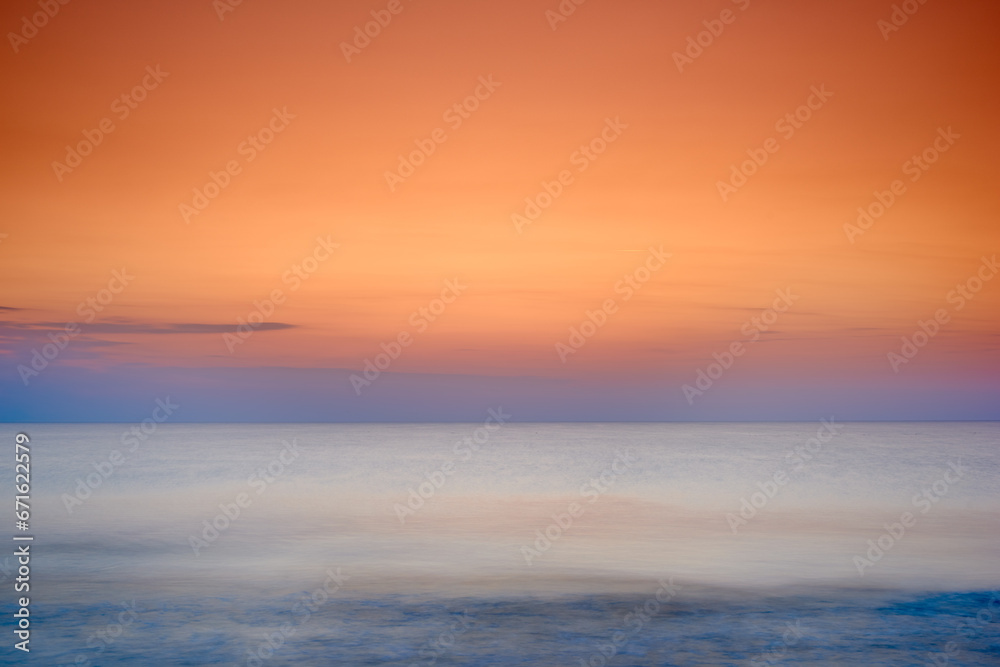 Copyspace seascape of an orange sunset on the west coast of Jutland in Loekken, Denmark. Sun setting on the horizon on an empty beach at dusk over the ocean and sea at night. Sunrise in the morning