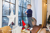 A 2-year-old boy sits on the windowsill in the new year. New Year's atmosphere at home. The child is waiting for the new year.