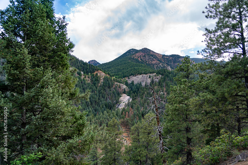 View of Stove Mountain from North Cheyenne Cañon Park in Colorado Springs, CO in the late afternoon on a sunny summer day, with trees, red rocks, and mountains in the landscape