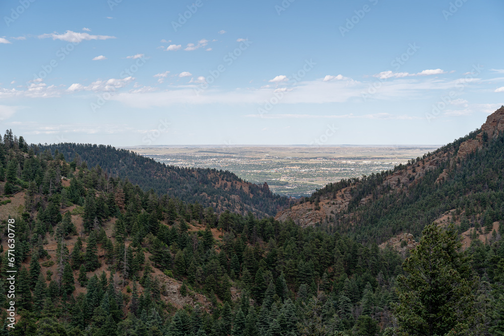 View from North Cheyenne Cañon Park in Colorado Springs, CO in the late afternoon on a sunny summer day, with trees, red rocks, and mountains in the landscape