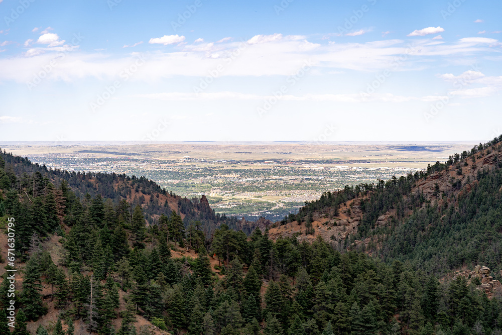 View from North Cheyenne Cañon Park in Colorado Springs, CO in the late afternoon on a sunny summer day, with trees, red rocks, and mountains in the landscape