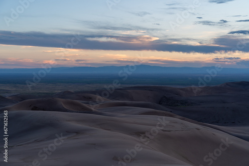 View from the top at golden hour and sunset at Great Sand Dunes National Park in Colorado on a sunny summer evening, with mountains in the background