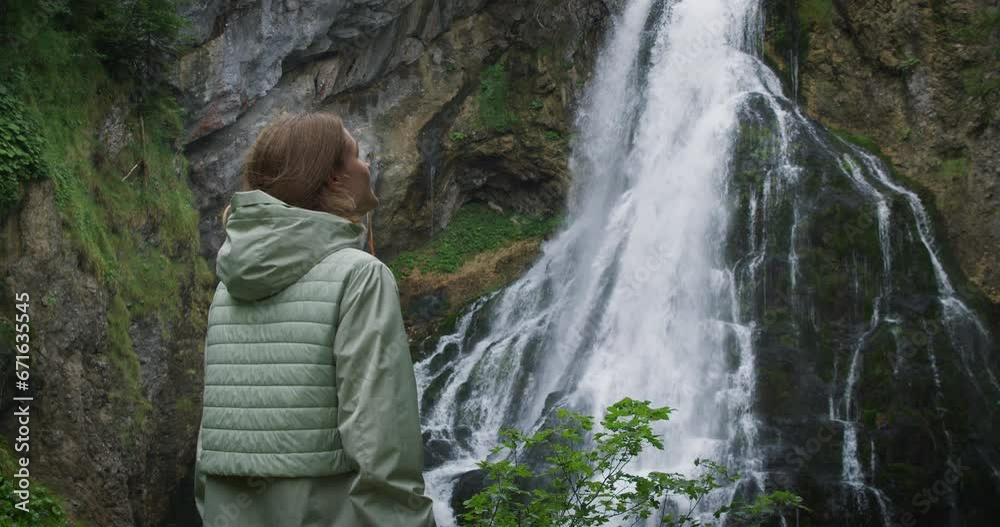 Woman enjoying a mighty waterfall at rainy day. Girl traveler in autumn coniferous forest. Gollinger Wasserfall in Austria. Woman enjoying a mighty waterfall at rainy day. Girl traveler in autumn coniferous forest. Gollinger Wasserfall in Austria.