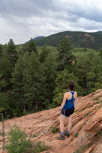A young women looks at evergreen trees and orange red rocks from Section 16 and Palmer Loop Hiking Trail in Colorado Springs, CO on a cloudy and overcast summer day