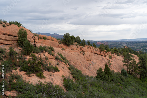 View of mountains, trees, and red rocks from Section 16 and Palmer Loop Hiking Trail in Colorado Springs, CO on a cloudy and overcast summer day - with Garden of the Gods in the background