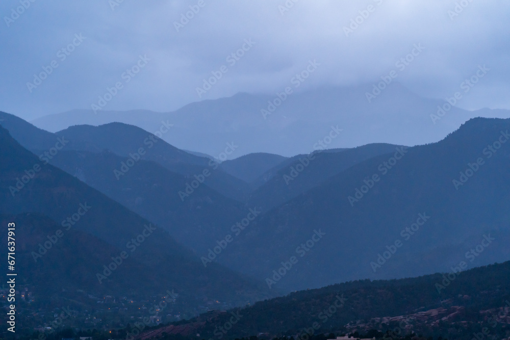 A view of a rainstorm over Pike's Peak and other blue misty mountains on a cloudy summer evening, as viewed from Garden of the Gods in Colorado Springs, CO