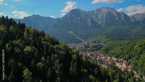 Astonishing aerial view with the rocky mountains filmed in cinematic style. Romanian landscape above Busteni city in a sunny day with blue sky