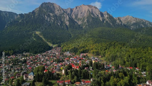 Astonishing aerial view with the rocky mountains filmed in cinematic style. Romanian landscape above Busteni city in a sunny day with blue sky photo