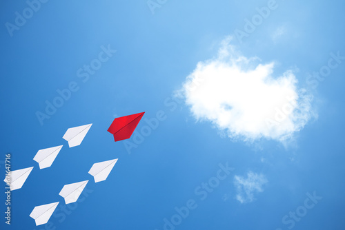 Red paper plane flying leads white paper planes on the sky. The leadership idea for working organizations and businesses. Symmetry paper airplane flying on clear blue sky with white cloud.