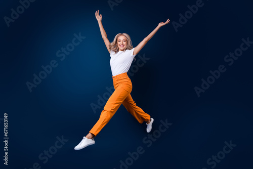 Full length photo of adorable cute girl gymnast wear trendy outfit jump up raise hands empty space isolated on dark blue color background