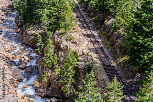 A railroad track runs beside a river in the Rocky Mountains in Colorado near Idaho Springs on a sunny day
