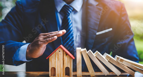 Businessman hand protect and stop wooden house from domino falling wooden bar for risk management and analysis of real estate concept for business.