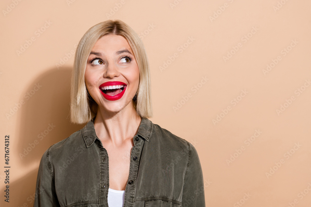 Photo of funny shocked lady open mouth overjoyed look empty space dreaming wear khaki shirt isolated beige color background