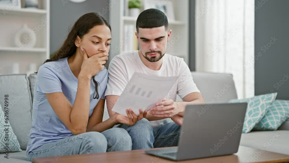 Stressed beautiful couple at home, reading upsetting document on laptop, worrying together in their living room Stressed beautiful couple at home, reading upsetting document on laptop, worrying together in their living room