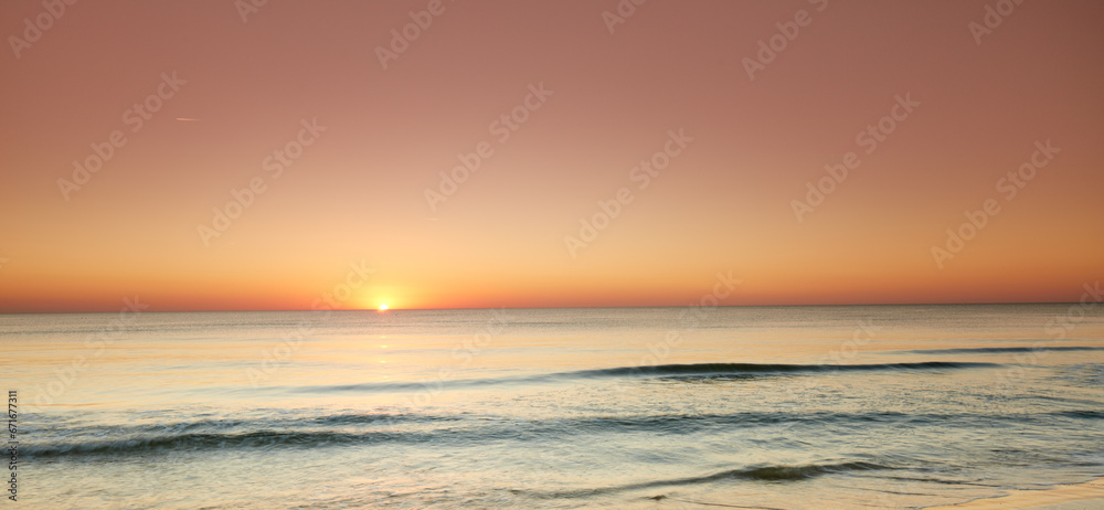 Seascape and landscape of a beautiful orange sunset on the west coast of Jutland in Loekken, Denmark. Sun setting on the horizon on an empty beach at dusk over the ocean and sea at night