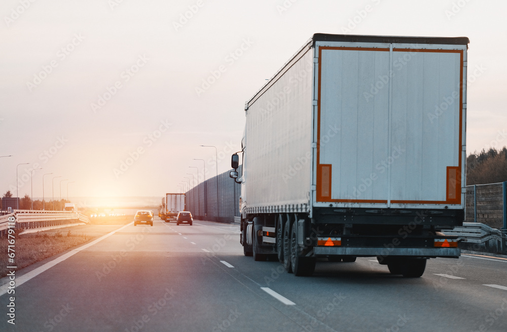 Modern white semi-trailer trucks on the highway driving in the right lane. Commercial vehicle for shipping and post delivery. Shipping of the goods on land with a door-to-door delivery process. Modern white semi-trailer trucks on the highway driving in the right lane. Commercial vehicle for shipping and post delivery. Shipping of the goods on land with a door-to-door delivery process.