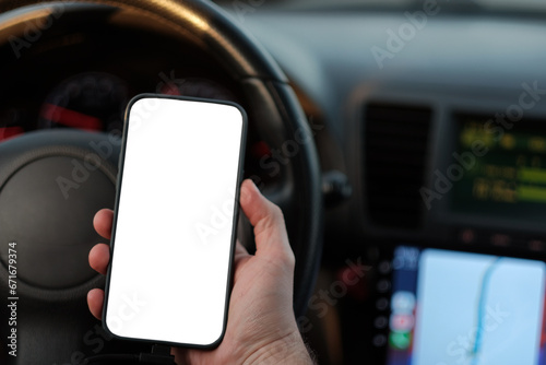 A man on driver seat holding a mock-up of a smartphone in the hand. Blank display of the touchscreen in the hand
