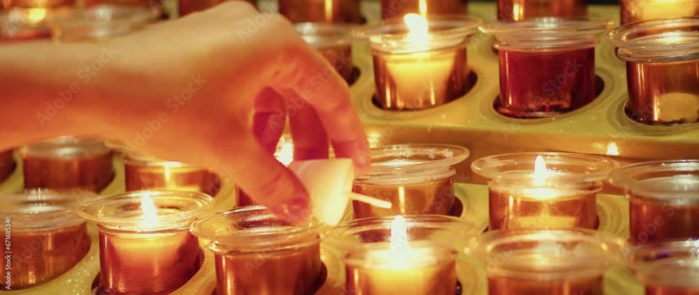 Close-up of woman hand holding candle and lighting it from another burning candle in church.