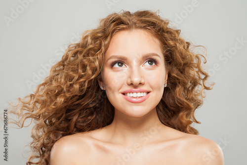 Attractive smiling female model with long natural healthy brown curly hair and cute smile looking up on white background. Hair care, hair treatment, wellness and cosmetology concept