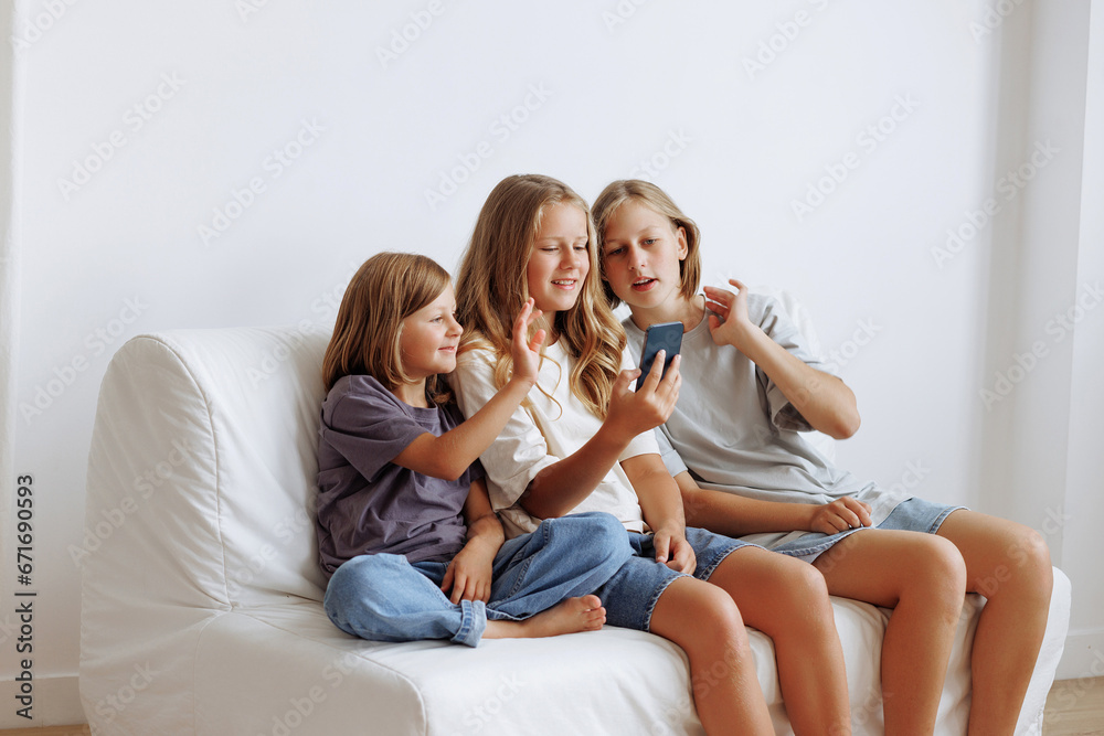 Three girls use smartphones on the sofa. Three sisters smiling in casual clothes against a white wall. Concept for advertising a mobile application or content for the whole family.