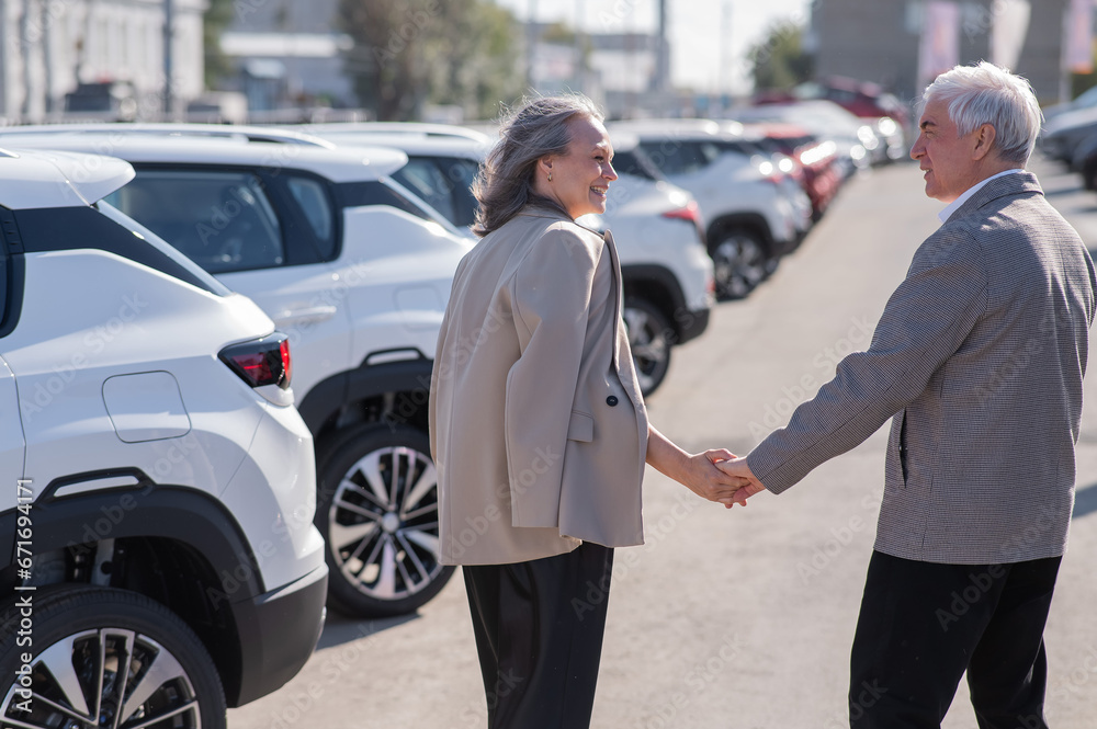 Mature Caucasian couple walks past cars outdoors, choosing a new one. 