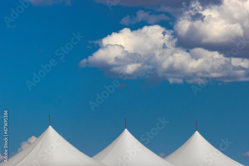 Clouds float over the tops of white tents in blue sky.