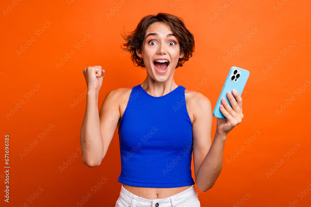 Photo of lucky impressed lady wear blue singlet rising fist online discount shopping modern device isolated orange color background