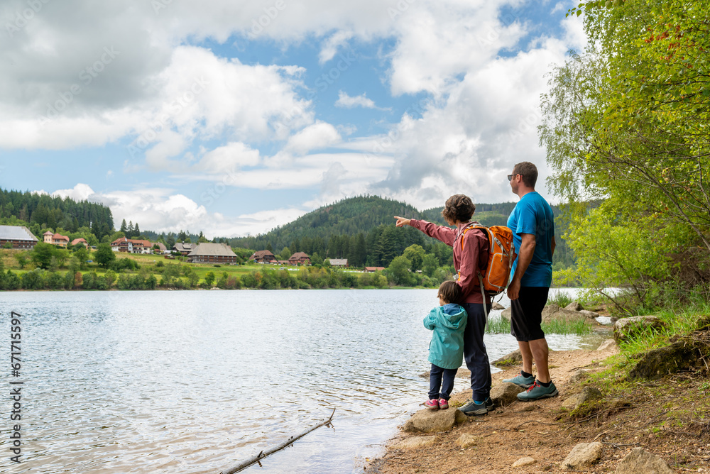 Mother, father and their little daughter at a lakeshore pointing Schluchsee village in Black Forest, Germany. Mother, father and their little daughter at a lakeshore pointing Schluchsee village in Black Forest, Germany.