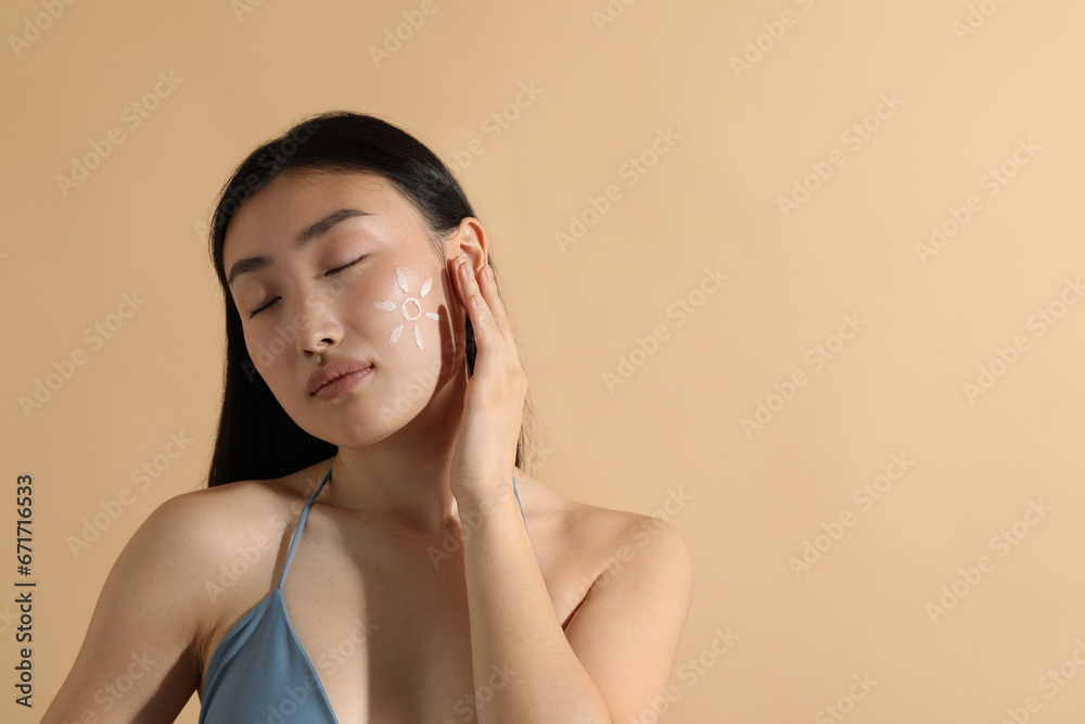 Fototapeta premium Beautiful young woman with sun protection cream on her face against beige background, space for text