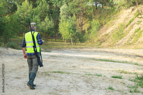 Man with hunting rifle wearing safety vest outdoors, back view. Space for text