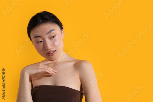 Beautiful young woman with sun protection cream on her face against orange background, space for text