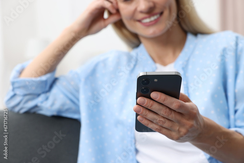 Happy woman sending message via smartphone at home, closeup