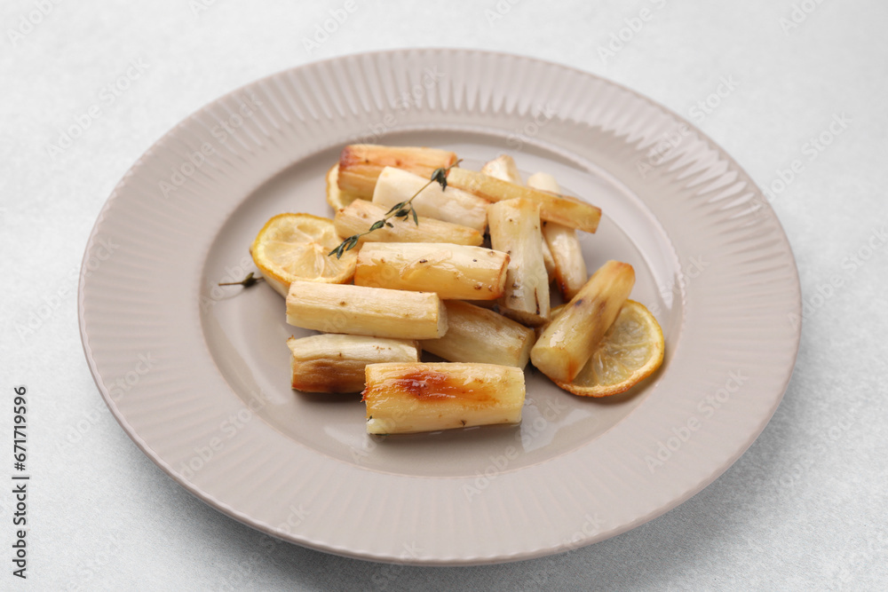Plate with baked salsify roots, lemon and thyme on light grey table, closeup Plate with baked salsify roots, lemon and thyme on light grey table, closeup
