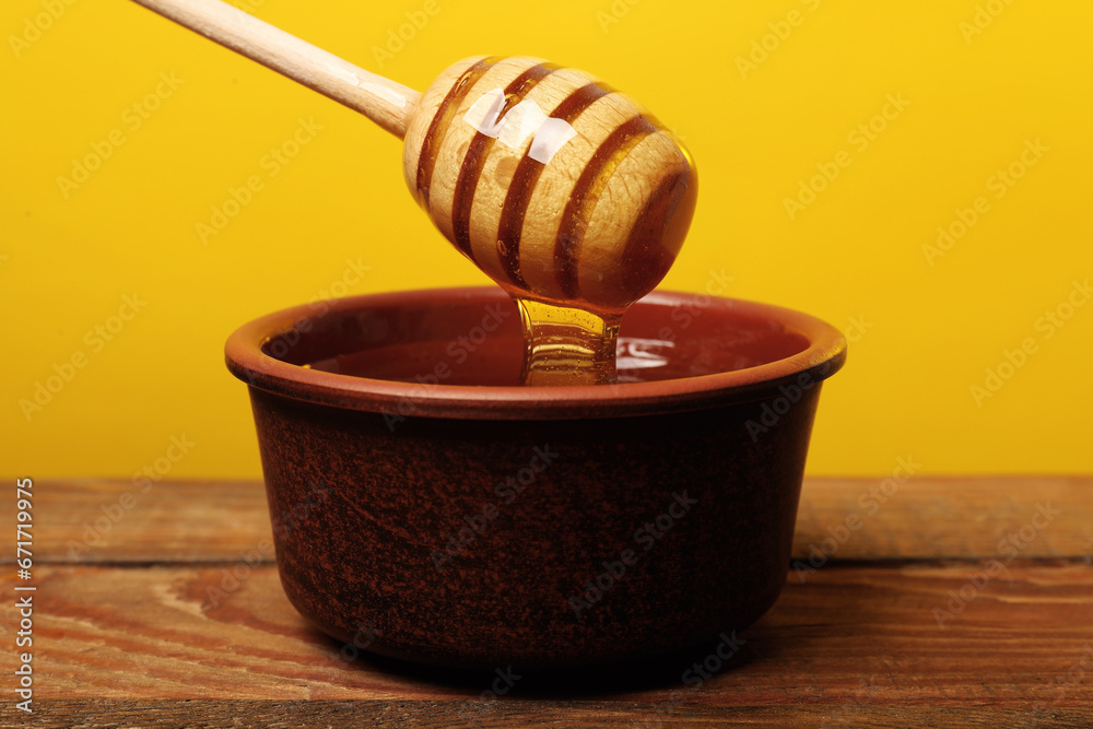 Pouring honey from dipper into bowl at wooden table against golden background Pouring honey from dipper into bowl at wooden table against golden background
