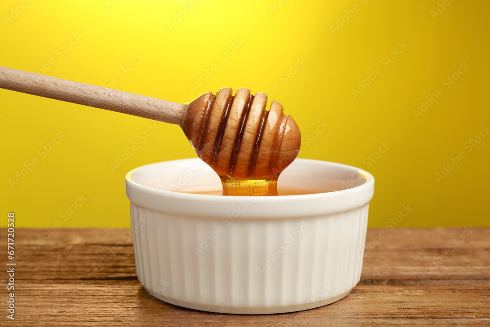 Pouring honey from dipper into bowl at wooden table against yellow background, closeup Pouring honey from dipper into bowl at wooden table against yellow background, closeup