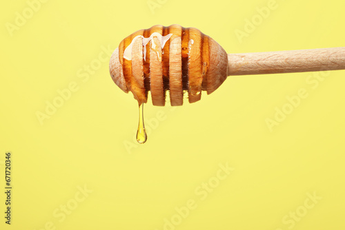 Delicious honey flowing down from dipper against yellow background, closeup. Space for text