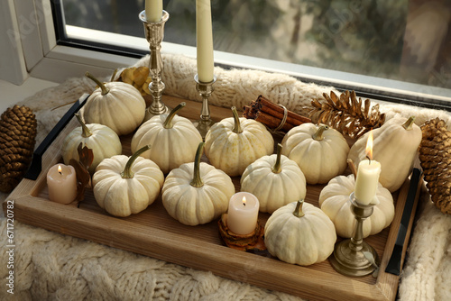 Tray with white pumpkins, cinnamon and burning candles on window sill indoors