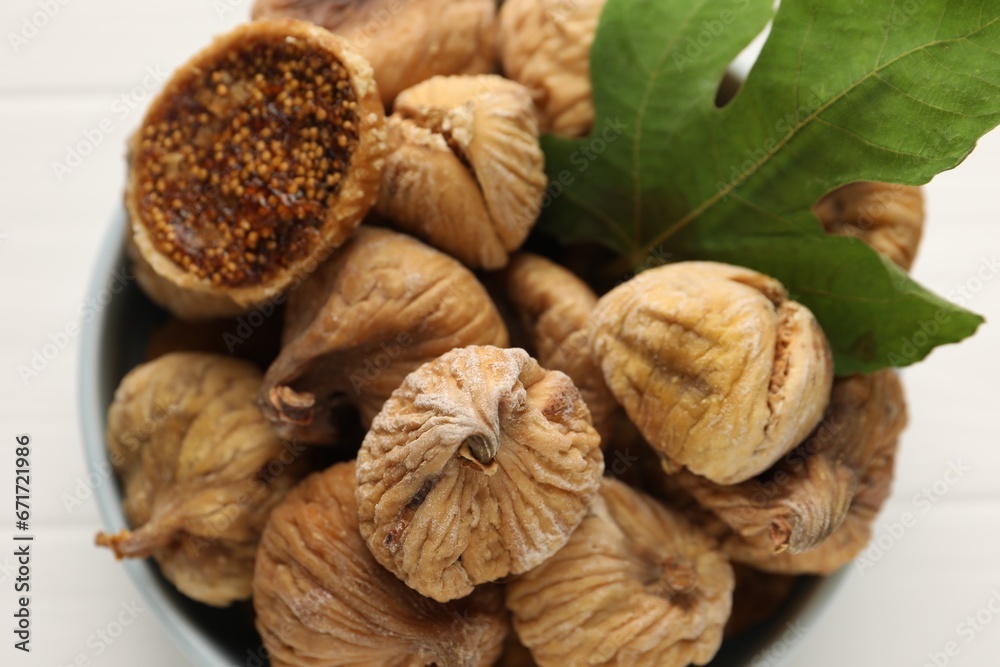 Bowl with tasty dried figs and green leaf on white table, top view Bowl with tasty dried figs and green leaf on white table, top view