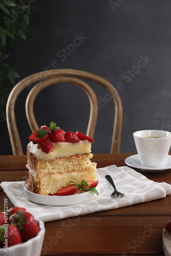 Piece of tasty cake with fresh strawberries  mint and cup of tea on wooden table