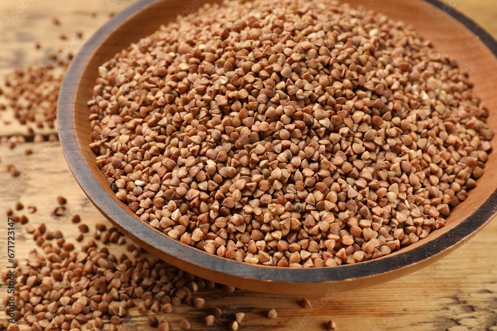 Bowl with dry buckwheat on wooden table, closeup
