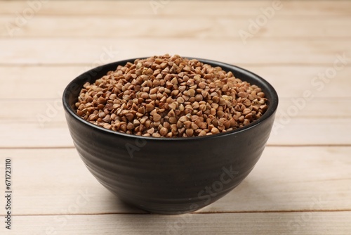 Bowl with dry buckwheat on light wooden table, closeup