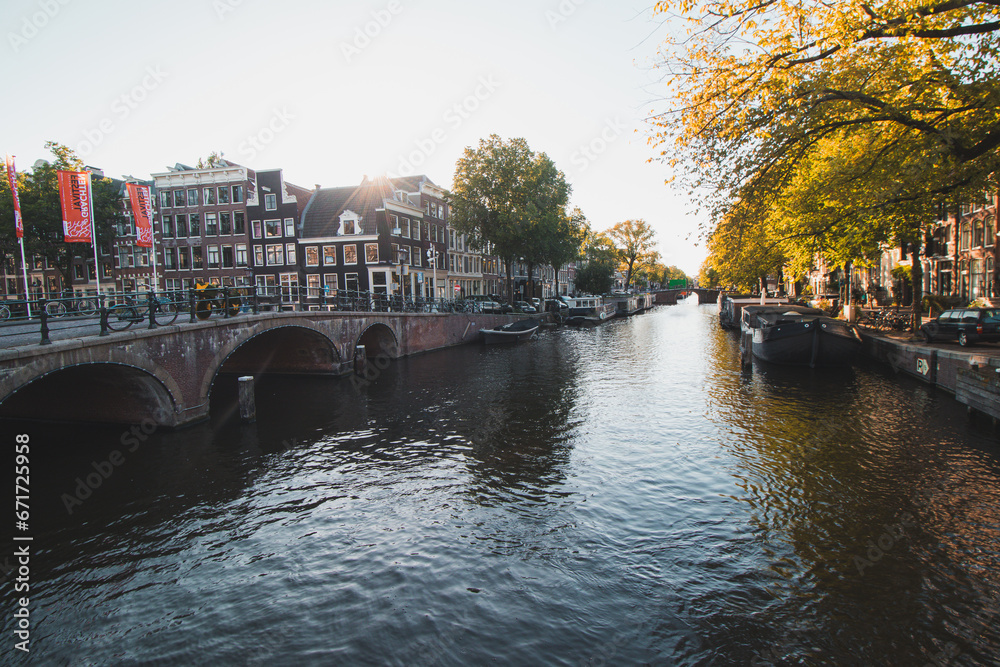 Naklejka premium Sunset illuminates a water canal and adjacent buildings in the capital city of Amsterdam, the Netherlands. Venice of the North