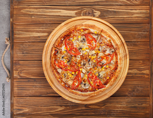 delicious pizza with chicken, mushrooms, cheese, tomatoes and corn on a wooden background